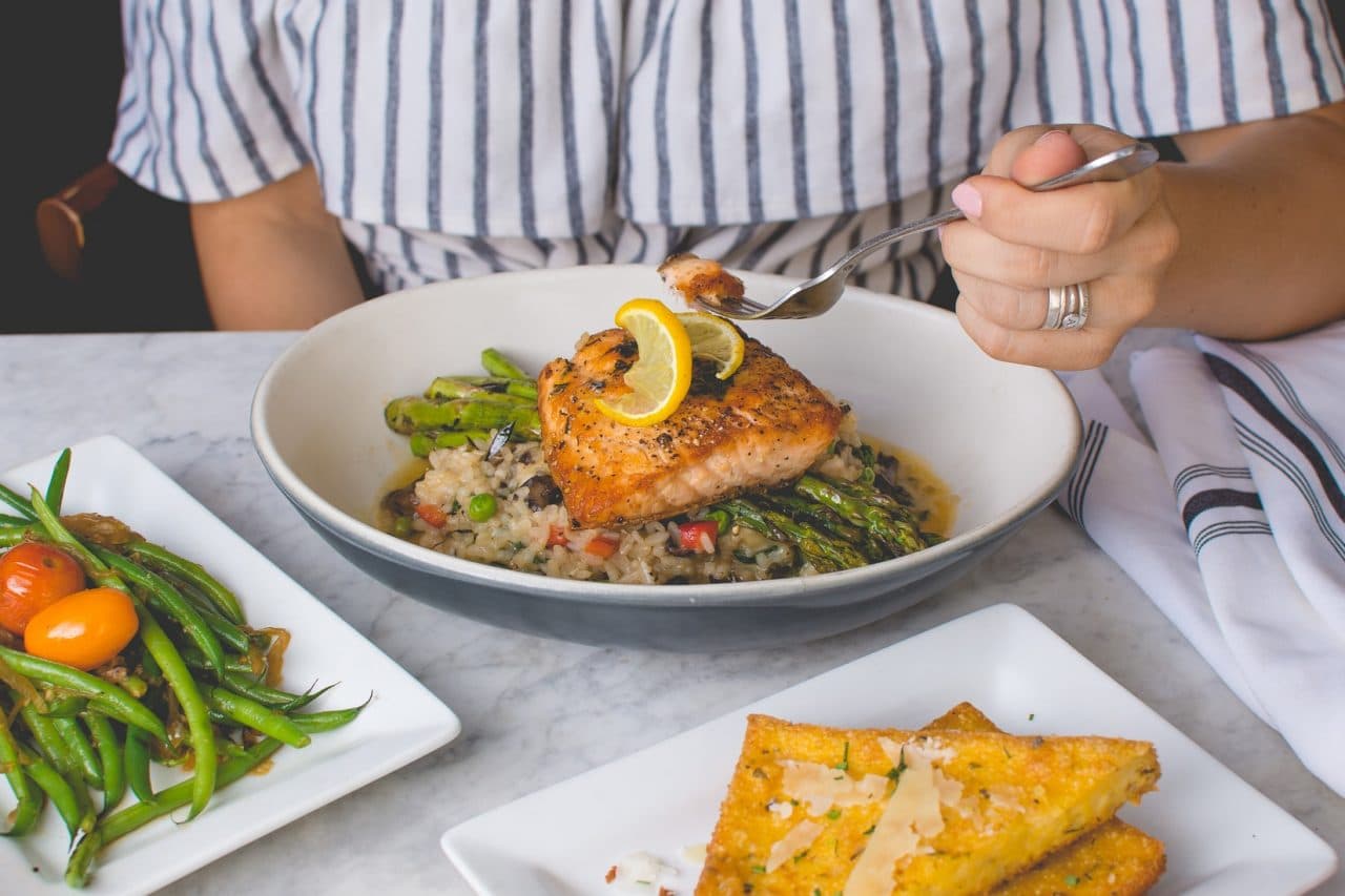 Someone eating a fish dinner with vegetables at a table.