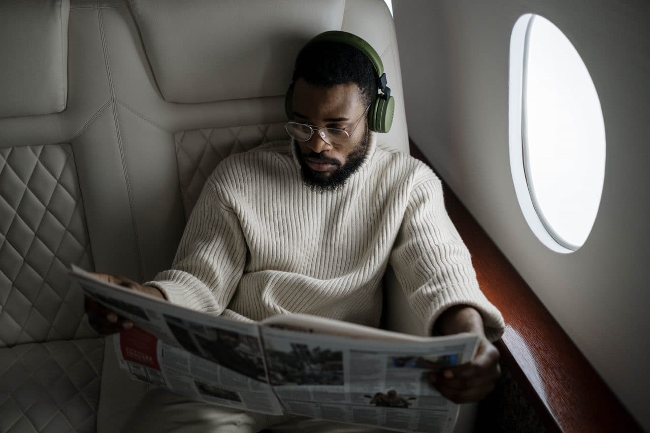 Man wearing noise-canceling headphones and reading the paper on his flight.