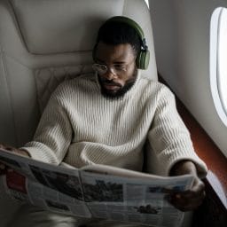 Man wearing noise-canceling headphones and reading the paper on his flight.