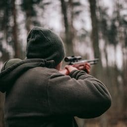 A man hunting with a rifle in the woods.