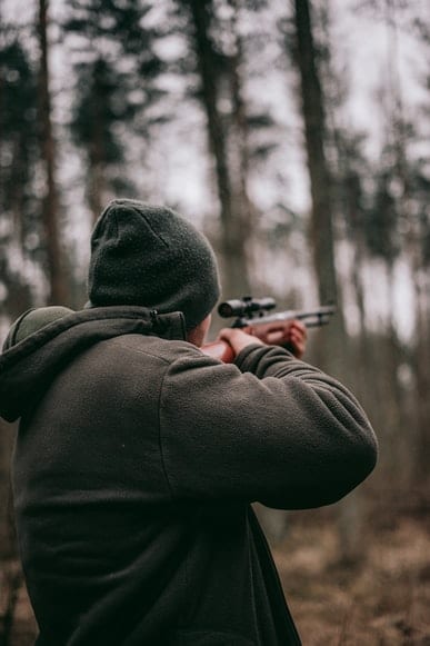 A man hunting with a rifle in the woods.