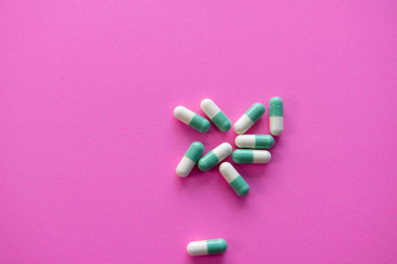 A pile of over-the-counter pills against a pink background.