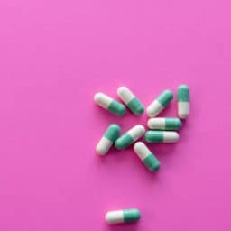 A pile of over-the-counter pills against a pink background.